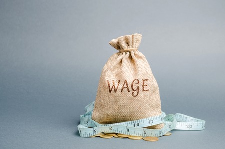 Money bag with the word Wage and tape measure. Wage cuts. The concept of limited profit. Lack of money and poverty. Small income. Salary reduction. Unsuccessful business. Financial crisisの写真素材