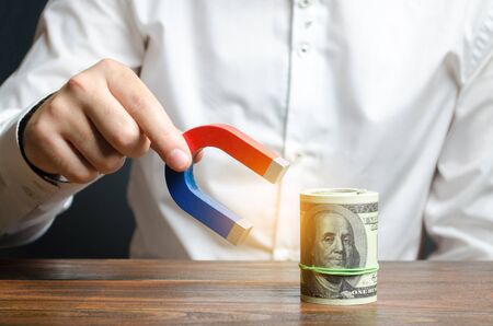 Businessman attracts money with a magnet. Attracting money and investments for business purposes and startups. Increase profits and attract new customers. Salary, bonus, cashback. Business strategy.の写真素材