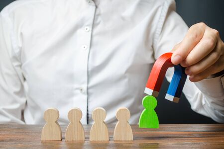 The businessman draws a green figure from the team with a magnet. Increase team efficiency and productivity. Identification of the most promising and talented workers. Promoted to the post of head.の写真素材