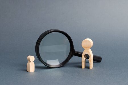 A wooden figure of a woman with emptiness and a child stands near the magnifying glass. The concept of finding a child, the adoption of children. Mother lost her baby and is now looking for him.の写真素材
