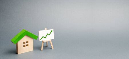 Wooden house and stand with red arrow up. Growing demand for housing and real estate. The growth of the city and its population. Investments. rising prices. banner, place for text. Selective focusの写真素材