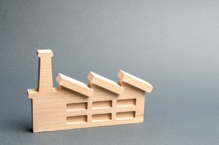 Wooden figurine of a plant or factory on a gray background. Recycling raw materials. The concept of industry and production.Investments in the construction of new factories.の写真素材