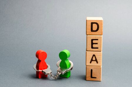 Two people are handcuffed to each other stand near a word deal. Unclosed obligations between two persons, financial or moral debt. Contract, duty, responsibility and duty. Keep the word, keep promise.の写真素材