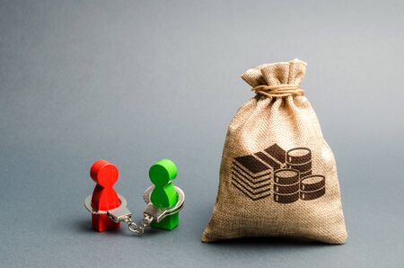Two people are handcuffed to each other and stand near a money bag. Unclosed obligations between two persons, financial or moral debt. refusal to return debts. redemption and restructuring.の写真素材