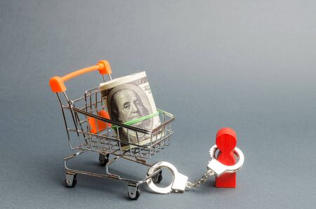 Person is handcuffed to a bundle of money on a supermarket cart. A person is limited by the burden of a large debt or liabilities, an outstanding loan and mortgage, a difficult financial situationの写真素材