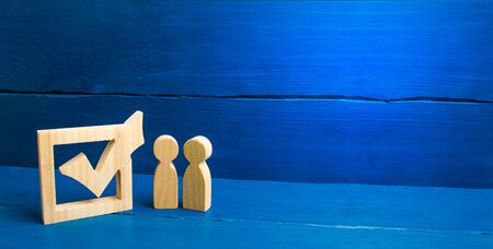 Two figures stand together next to tick in the box. The concept of elections and social technologies. Volunteers, parties, candidates, constituency electorates. Selective focus banner, place for textの写真素材
