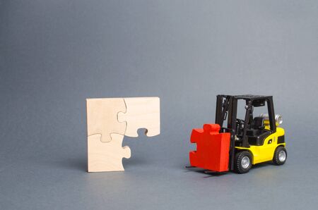 The yellow forklift truck brings the missing red puzzle to the unfinished construction. Completion of project, a key element. Creating new, teamwork. Planning and investment. Startup, crowdfundingの写真素材