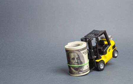 Yellow forklift truck can't lift a huge bundle of dollars. Expensive loans, high tax burden. attracting investment. High costs and barriers to business. Improving business processes and logisticsの写真素材