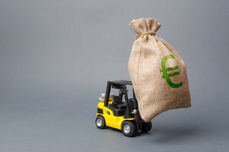 Yellow forklift truck carries a big bag of money. Attracting investment in development, modernization of production and business. Revenue, profit, liquidity. profit point fixation. capital migrationの写真素材