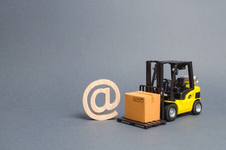 Yellow Forklift truck carries a cardboard box near a email symbol commercial AT. development of Internet network trade. E-commerce. sales of goods through online trading platforms. shopping online.の写真素材