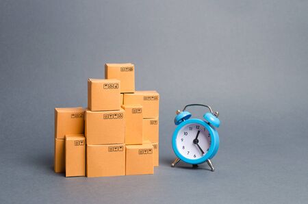 Lots of cardboard boxes and a blue alarm clock. Express delivery concept. Temporary storage, limited offer and discount. Optimization of logistics and delivery, improving transportation efficiencyの写真素材