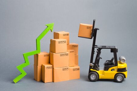 Yellow Forklift truck raises a box over a stack of boxes and a green arrow up. High trade volumes, increased production, storage infrastructure. raise economic indicators. exports, imports. sales riseの写真素材