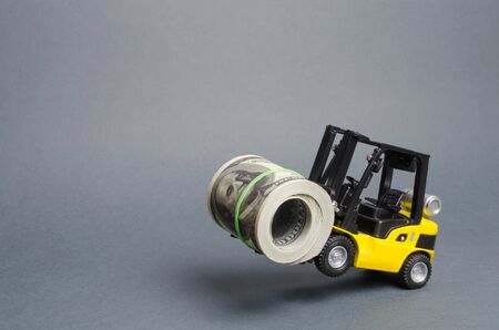 A yellow loader stands on the rear wheels holding a big bundle of dollars. concept of attracting investment, issuing concessional loans for business development. High profitability of stocks and bondsの写真素材