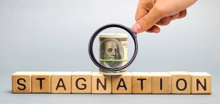 Wooden blocks with the word Stagnation and dollars. Prolonged period of slow economic growth, measured in terms of GDP growth. High unemployment. Economic stagnation. Performance slowdownの写真素材