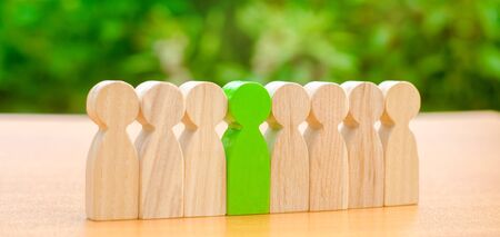 Wooden figures of people. Green man stands out from the crowd of workers. The concept of choosing a new leader. Choice of person. Hiring and recruiting. Talented employee. Demote. Selective focusの写真素材