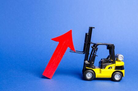 A yellow forklift raises a big red arrow up. Growth in production rates and development of industry and infrastructure. Increased sales, economy growth. Concept of increase, growth and success.の写真素材