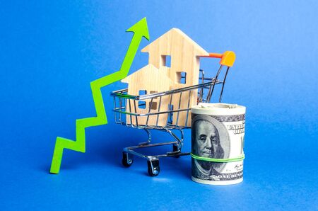 Two wooden houses in a trading cart and green arrow up and money bundle. Increasing cost and liquidity of real estate. Attractive investing. rising prices or renting. growth demand, rates of sales.の写真素材