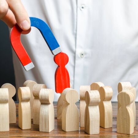 businessman pulls out a red figure of a man from the crowd with the help of a magnet. leader manages the business and forms a team. Increase team efficiency, productivity. toxic, non-competent worker.の写真素材