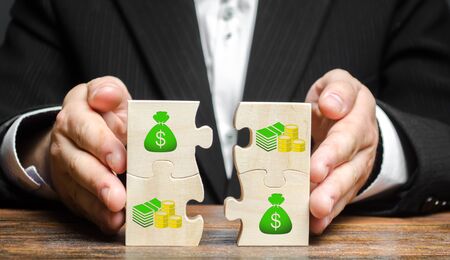 Businessman combines money puzzles. Fundraising, attracting investments for the implementation of business projects and startups. Crowdfunding. Accumulation of resources and money, opening a business.の写真素材