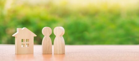 Two wooden figures of people and a house on a nature background. concept of affordable housing, mortgages for buying a home for young families and couples. Family nest. Copy space. Bannerの写真素材