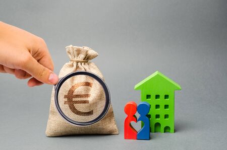 Money bag and family standing near the house. The concept of money management and property. Budget planning. Accumulation of money for a home or apartment. Mortgage, taxes and debts. Creditの写真素材