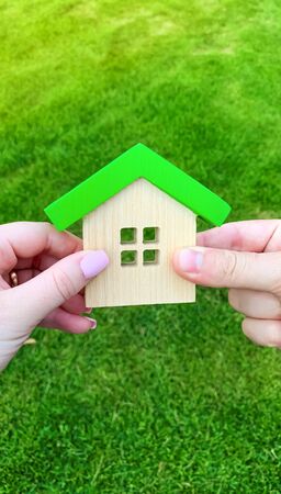 Wooden house in the hand of a young family. Buying a home in a mortgage loan. Real estate concept. Eco friendly home. Government support. Symbol of happy family life. Buying a housing outside the cityの写真素材