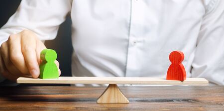 Wooden figures of people on scales and a mediator / arbitrator. Resolving conflict situations and disputes. Conclusions of the peaceful resolution of disputes. Conflict of interest. Business opponentsの写真素材