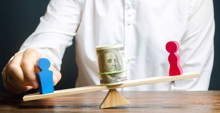 Wooden figures of man and women on the scales. Concept of gender pay gap. Income inequality. Oppression of women. Gender discrimination. Underestimation of female labor. Segregation.の写真素材