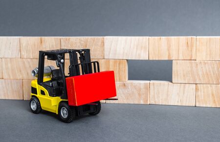 A forklift carries a red block to insert into a wall void. A key element to complete the project, part of the whole. Innovation, concept of idea. Cooperation and collaboration. Teamworkの写真素材