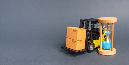 A forklift truck carries cardboard boxes and an sand hourglass. Express delivery in short time concept. Temporary storage. Optimization delivery logistics Transport company. Performance efficientの写真素材