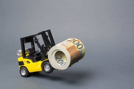 A yellow loader stands on the rear wheels holding a big roll bundle of Euro. concept of attracting investment, issuing concessional loans for business development. High profitability of stock bondsの写真素材