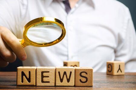 A journalist holds a magnifying glass over the word News. Review the main events and analytics. Fake news. Information. The most important events in the country and the worldの写真素材