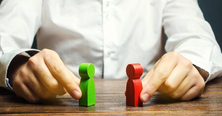 A man holds in his hands the red and green figures of people facing each other. The search for a compromise, mediation in negotiations. Weave intrigue. Conflict resolution, conflict of interest.の写真素材
