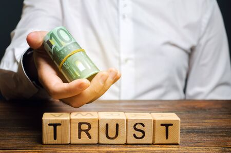 Wooden blocks with the word Trust and money in the hands of a businessman. Trust relationships...