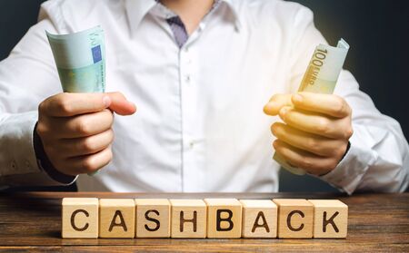 Wooden blocks with the word Cashback and money in the hands of a businessman. Bonus program to attract customers and increase their loyalty. Internet Commerce and banking. Cash back. Percentageの写真素材