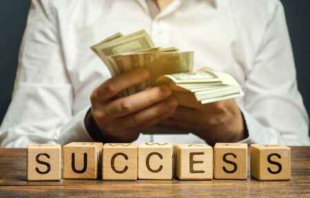 Wooden blocks with the word Success and businessman with money. Successful business concept. The growth of profits and earnings. Performance. Achieving the goal. Return on investment and profitabilityの写真素材