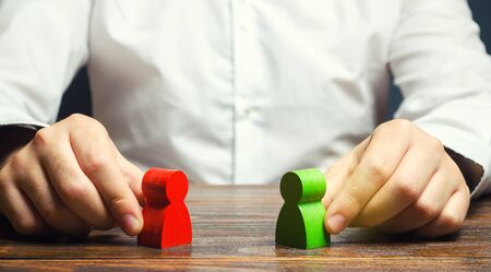 A man holds in his hands the red and green figures of people facing each other. The search for a compromise, mediation in negotiations. Weave intrigue. Conflict resolution, conflict of interest.の写真素材