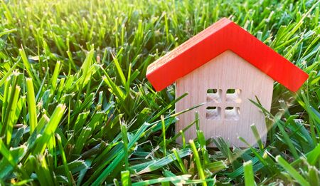 Miniature wooden house on grass. Real estate concept. Eco-friendly and energy efficient house. Buying a home outside the city. The urban downshift. Nature. Fresh air. Mortgage, loan. Red roofの写真素材