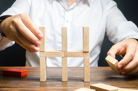 Businessman collects a house of dominoes. Conceptual creation of a new business or startup, establishing processes. Construction of a residential building. Mortgage. Real estate market and investment.の写真素材