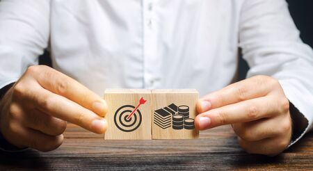 Businessman collects wooden blocks with the image of the goal and money. The concept of doing business and finance. Setting goals and objectives for maximum profit. Strategy and Planningの写真素材