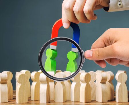 A magnifying glass looks at a magnet pulls green figures of people out of the crowd. Recruiting new...