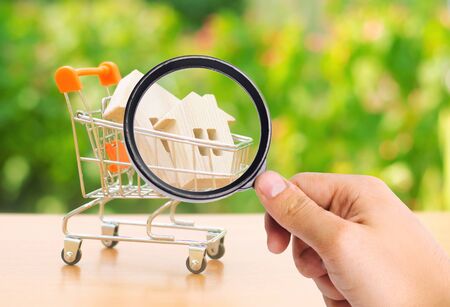 A magnifying glass looks at a wooden house in a trading cart on nature background. The concept of buying and selling real estate, renting. Attractive investing. rising prices. supply and demandの写真素材
