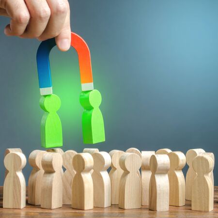 A hand with a magnet pulls green figures of people out of the crowd. Recruiting new workers. Formation of a new team. Search for right people and talented workers with great career potential.の写真素材