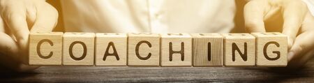 Wooden blocks with the word Coaching in the hands of a man. Self improvement. Achieving goals through training and guidance. Coach. Skills development. Training course.の写真素材