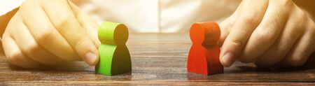 A man holds in his hands the red and green figures of people facing each other. The search for a...