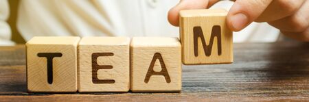 Businessman holds wooden blocks with the word Team. Team management concept. Teamwork. Hiring. Recruitment staff. Work in cooperation. Leadership skills. Analysis and analytics business processの写真素材