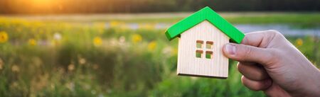 Wooden house in the hands in the sunset background. Real estate concept. Eco friendly home. Symbol of happy family life. Buy a housing outside the city. Search for hotel on vacation. Selective focusの写真素材