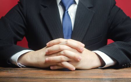 A man sits at the table with folded arms. Ready to listen to news and criticism. Serious talk. Calmly. Communication and body expressions. Job interview. Make an informed decision. Humility.の写真素材