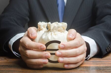 Businessman embraces euro money bags. Financing business project or education. Trade, economics. Corruption. Provision financial loan credit. Bank deposit. Budget, tax collection. Subsidies, savings.の写真素材
