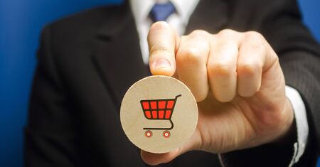 Businessman holds a wooden block with the image of a supermarket cart - shopping trolley. Retail and shopping. Ecommerce and delivery service concept. Marketing. Trade. Sale of productsの写真素材